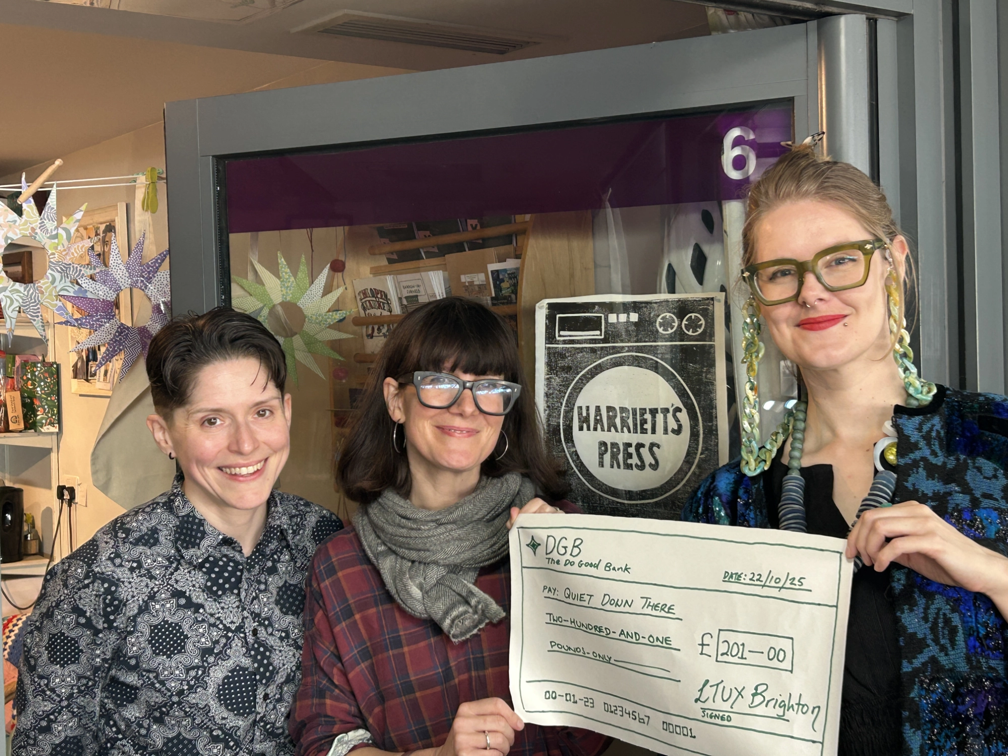 At Harriet's Press upstairs at the Brighton's Open Market. Fiona MacNeill and Heidi Swigon are handing a hand drawn cheque to Emily Atkinson from Quiet Down There.
