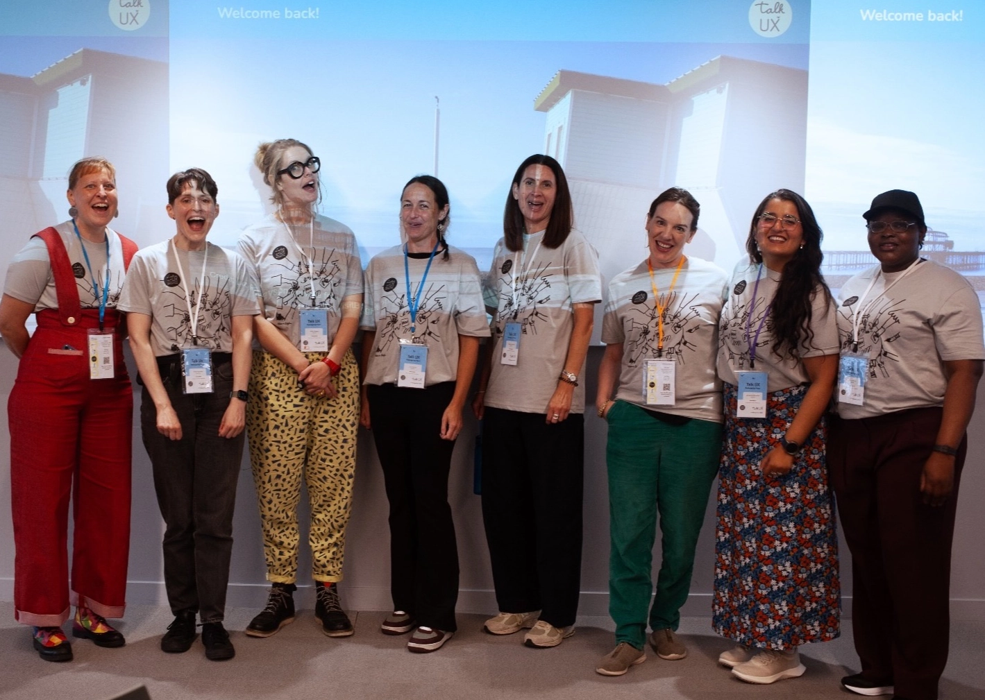 the group of organiser for Talk UX at the front of the main room, in front of a projected image showing the Brighton beach front.